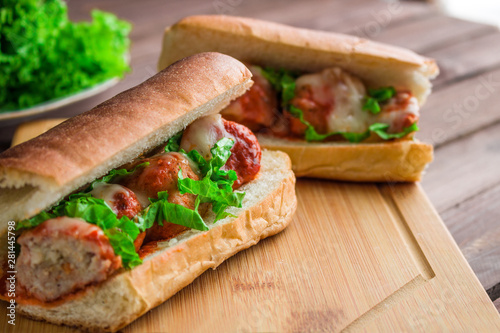 homemade meatball sub sandwich halves with mozzarella and lettuce on cutting board close up