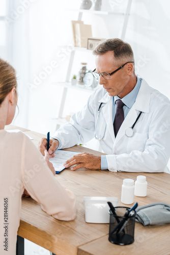 cropped view of woman near doctor in glasses writing diagnosis