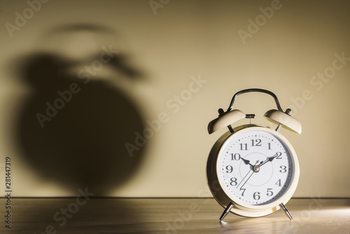 Alarm clock over wooden desk with shadow on wall