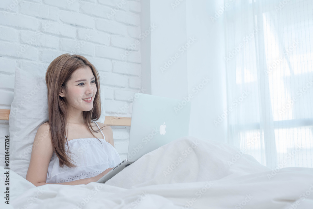 Happy  woman reading news as she relaxes in bed with a laptop computer in the morning