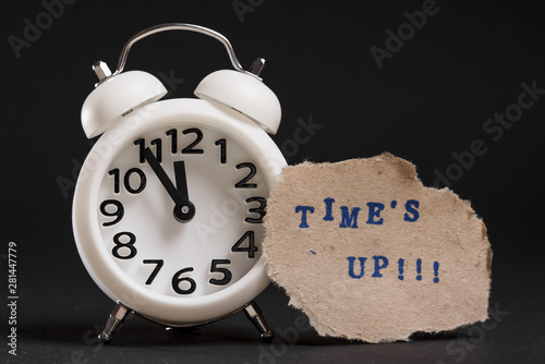 Times up text on torn brown paper near the white alarm clock against black background