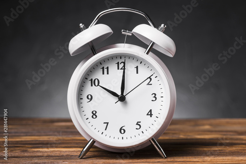 White alarm clock on wooden textured table showing 10'oclock