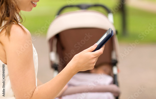 motherhood, leisure and technology concept - close up of happy mother with child in stroller reading internet book at summer park