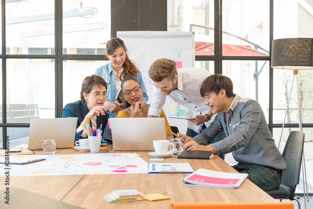 Group of five casual business meeting to discuss ideas and laptop on table in office.