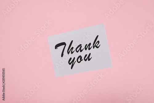 top view of white card with thank you inscription on pink background