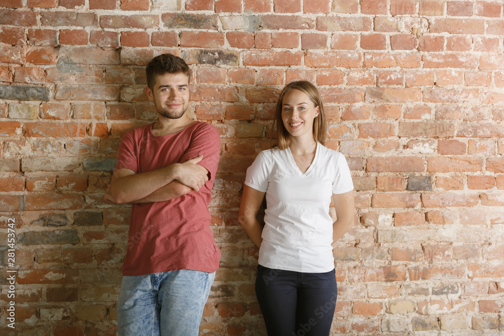Young couple preparing for doing apartment repair together themselves. Married man and woman before home makeover or renovation. Concept of relations, family, love. Standing against brick's wall.