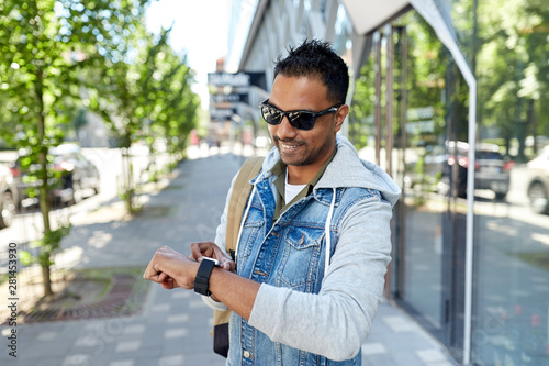 travel, tourism and lifestyle concept - smiling indian man with smart watch and backpack walking along city street