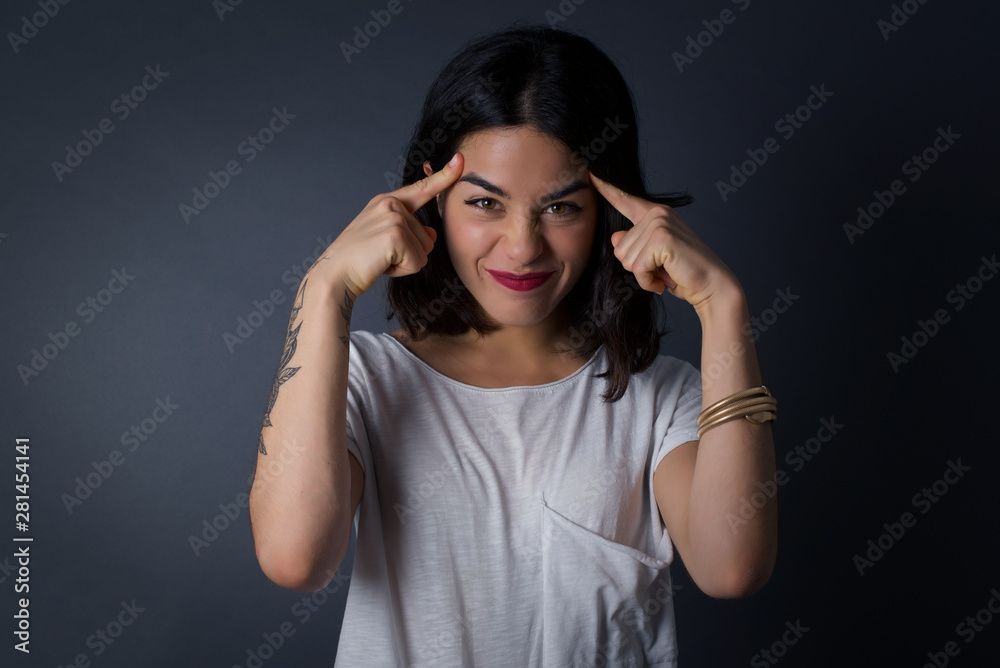 Young beautiful girl concentrating hard on an idea, with a serious look, thinking with both index fingers pointing to forehead eyes closed. Young beautiful girl concentrating hard on an idea, with a serious look, thinking with both index fingers pointing to forehead eyes closed.