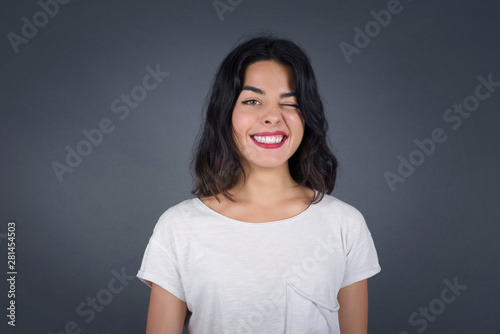 Cute young blonde female with long hair wearing White sweater blinking her eyes with pleasure having happy expression. Facial expressions and people emotions concept.