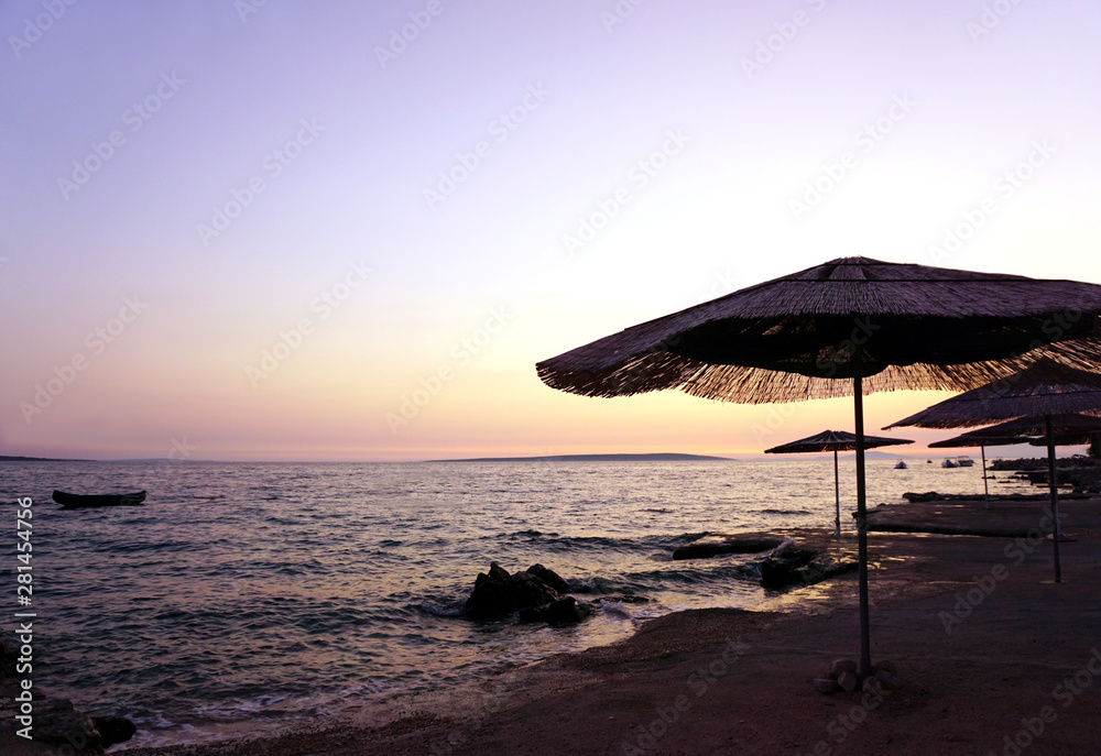Bamboo sun umbrellas on the empty beach by the sea on the sunset, with pastel color sky and sea Bamboo sun umbrellas on the empty beach by the sea on the sunset, with pastel color sky and sea