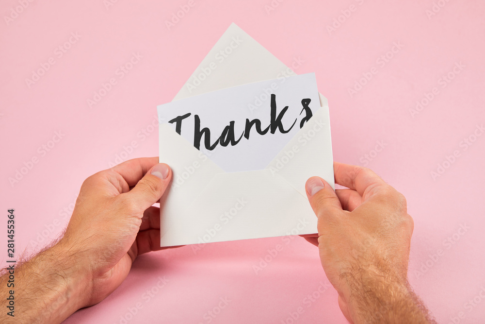 cropped view of man holding envelope and white card with thanks word on pink background cropped view of man holding envelope and white card with thanks word on pink background