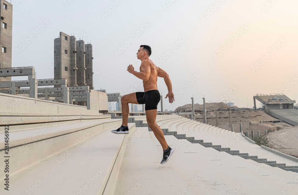 Muscular caucasian male athlete running up a stadium stairs on a hot summer day