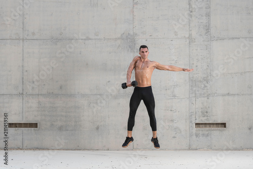 Muscular shirtless caucasian male athlete performs a dumbbell weightlifting exercise in a grungy concrete structure while showing his six pack abs  © Paul