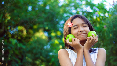 Happy littel asian girl hold oGreen appel in her hand wear white dress and Green leaf background. photo