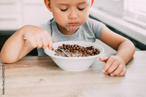 cute baby eating chocolate milk balls in the kitchen in the afternoon