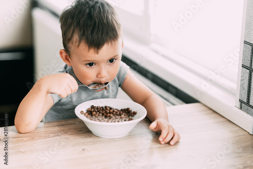 cute baby eating chocolate milk balls in the kitchen in the afternoon