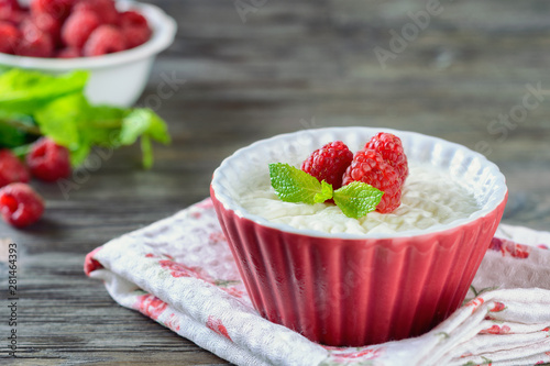 Delicious cream Panna Cotta dessert decorated with berries of raspberry and mint leaves in ceramic form on a wooden table next to the berries in a bowl, closeup