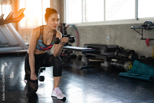 Young asian girl playing dumbbell to exercise in fitness.Slim woman lifts heavy dumbbell while training in the gym. Sports concept fat burning and a healthy lifestyle.