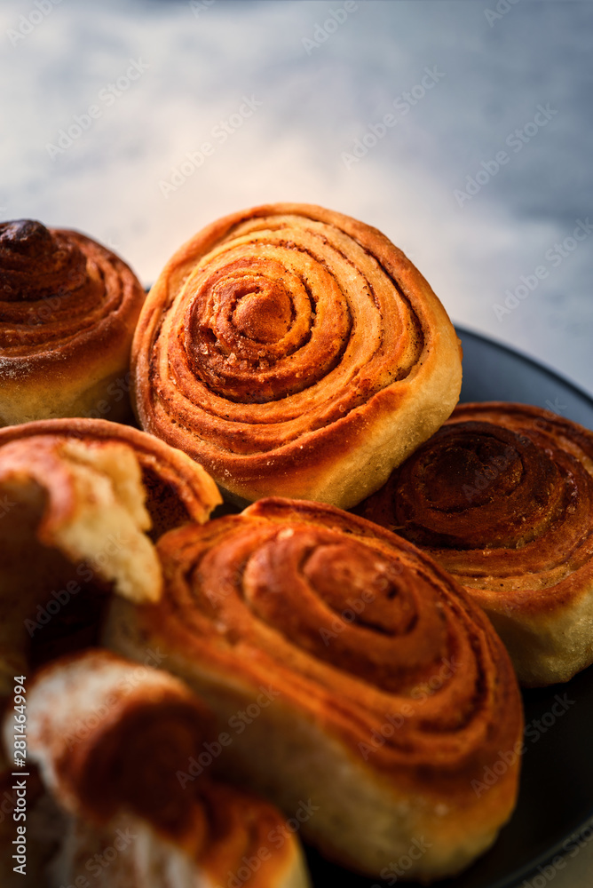 Handmade rolls with cinnamon on a dark dish and on a gray background.