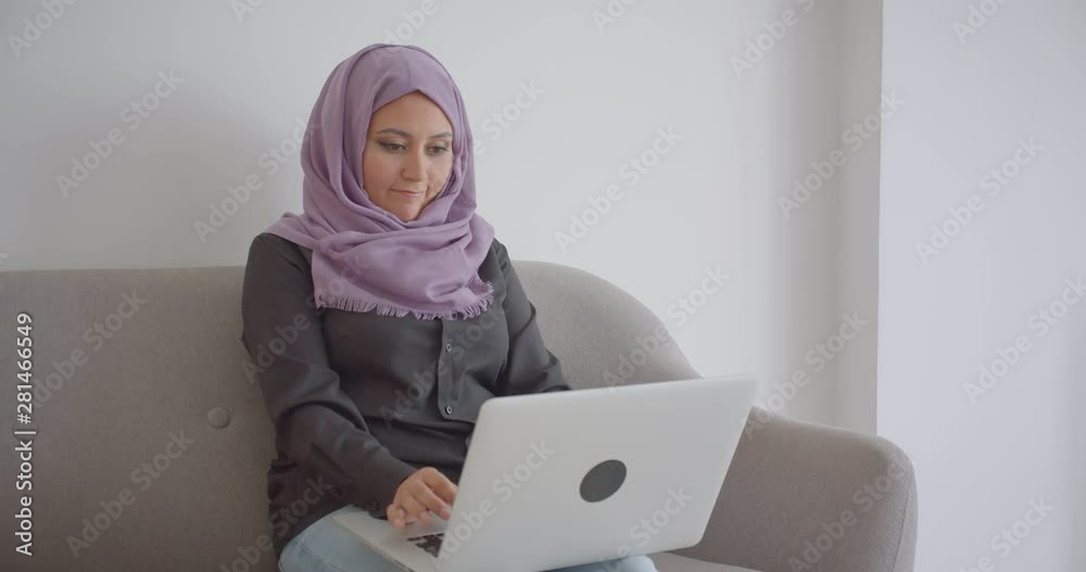 Closeup portrait of young muslim businesswoman in hijab using the laptop indoors in the apartment