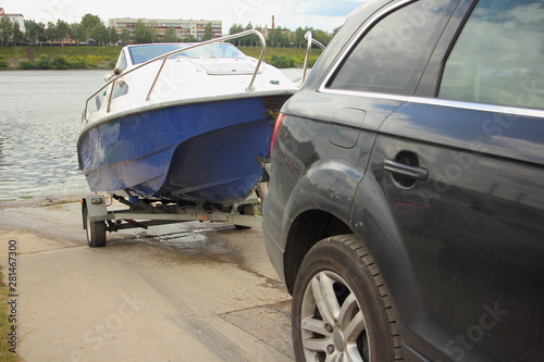 Obraz na płótnie A 4x4 black car pulls blue-white trimaran cabin motor boat on trailer on concrete slipway into the river water, DIY boat launch w salonie