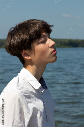 Portrait of a teenager, man, in a white shirt against a blue sky and a large lake.