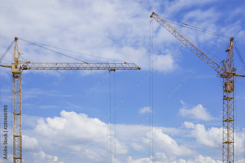 Copy space between two construction cranes against blue cloudy sky Copy space between two construction cranes against blue cloudy sky