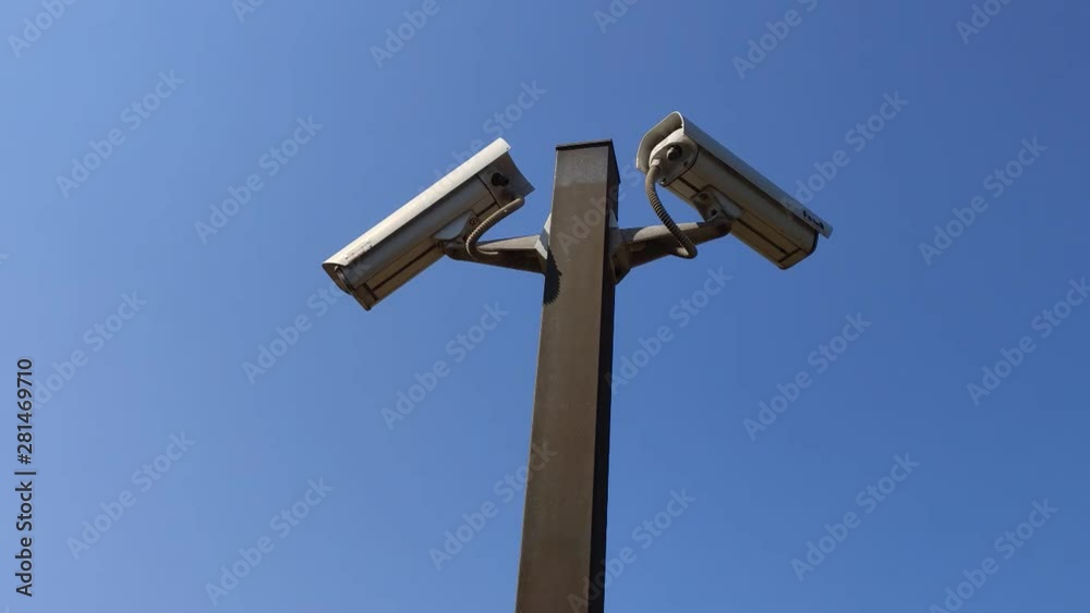 Two security cameras against the blue sky are monitoring, copy space. Two surveillance cameras against blue sky as background Two security cameras against the blue sky are monitoring, copy space. Two surveillance cameras against blue sky as background