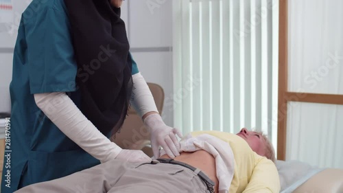 Tilt up of female Muslim doctor wearing hijab doing palpation of female patient abdomen