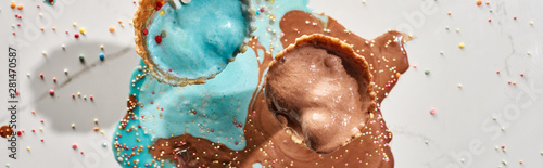 top view of delicious melted chocolate and blue ice cream in waffle cones on marble grey background with sprinkles, panoramic shot