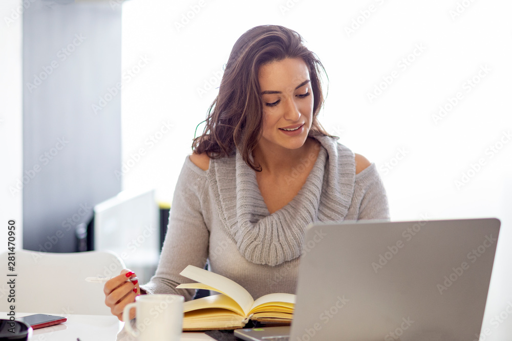 Beautiful woman sitting with laptop and coffee mug and note book on the table