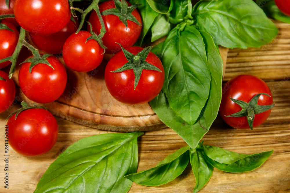 Fresh cherry tomatoes with green basil leaves on a wooden table Fresh cherry tomatoes with green basil leaves on a wooden table