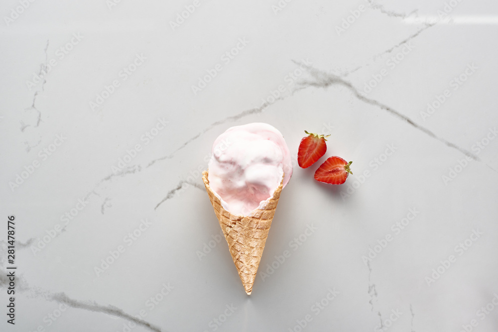 top view of tasty ice cream in waffle cone near strawberries on marble grey background