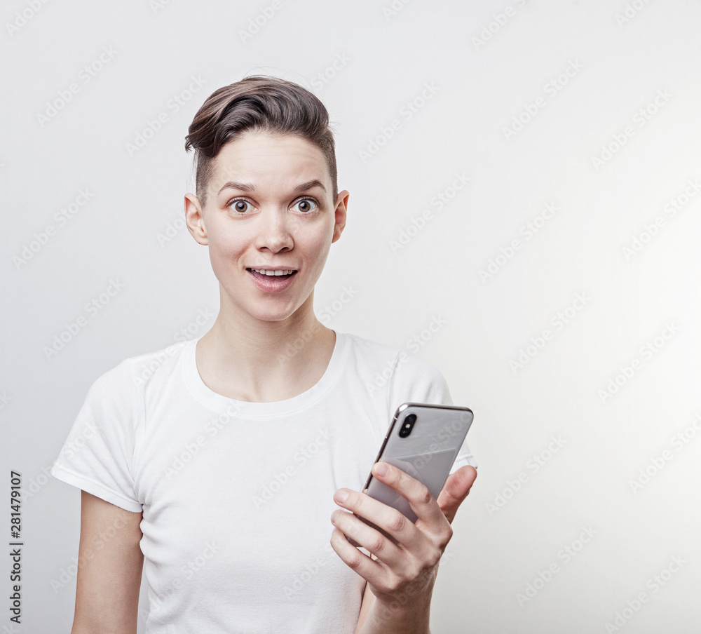 Happy funny millennial woman's celebrating win or victory, triumph, holding a phone. Cheerful excited girl, laughing, having fun, using cell phone apps. Isolated on white studio blank background. Happy funny millennial woman's celebrating win or victory, triumph, holding a phone. Cheerful excited girl, laughing, having fun, using cell phone apps. Isolated on white studio blank background.