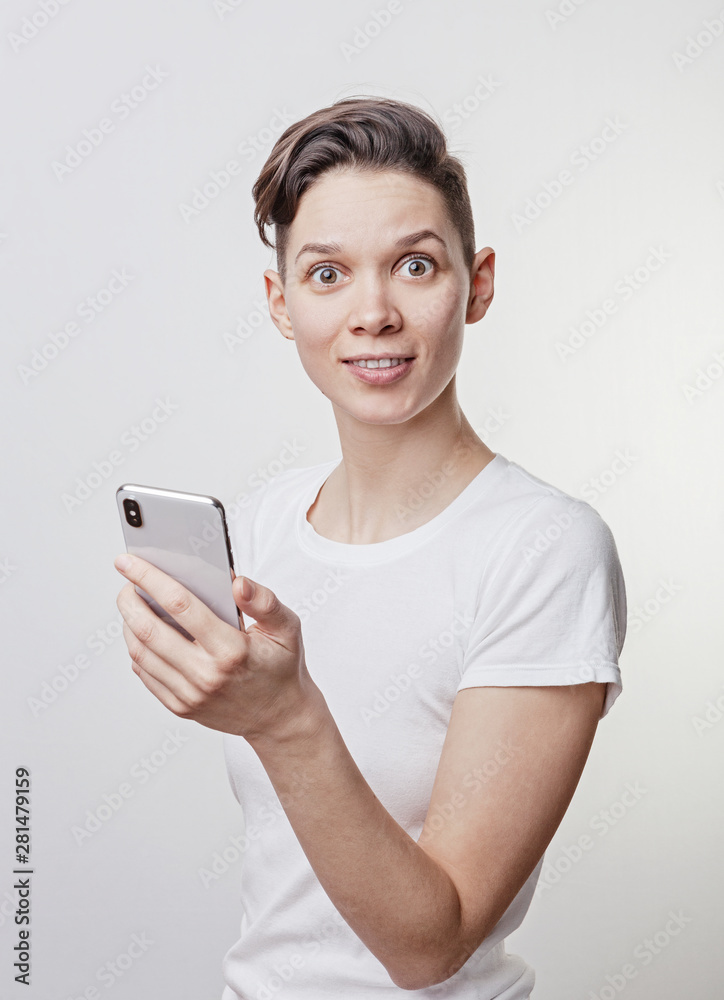Happy funny millennial woman's celebrating win or victory, triumph, holding a phone. Cheerful excited girl, laughing, having fun, using cell phone apps. Isolated on white studio blank background. Happy funny millennial woman's celebrating win or victory, triumph, holding a phone. Cheerful excited girl, laughing, having fun, using cell phone apps. Isolated on white studio blank background.