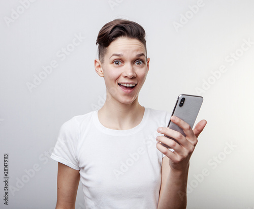 Happy funny millennial woman's celebrating win or victory, triumph, holding a phone. Cheerful excited girl, laughing, having fun, using cell phone apps. Isolated on white studio blank background.