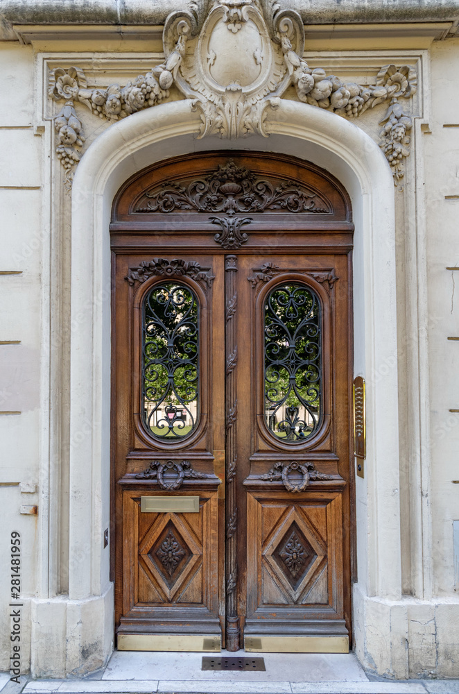 Baroque architecture of arch door entrance of antique building in Paris France. Vintage wooden doorway with ornate gratings and whimsical stone fretwork arch of ancient house with sculptural details.