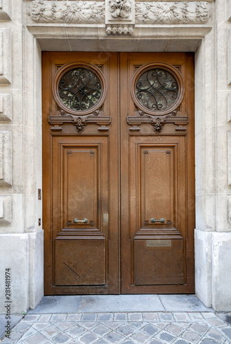 Double door entrance of historic building in Paris France. Vintage wooden doorway and stone fretwork decorations of stucco wall with sculptural details. Ornate carving wood door with round gratings.