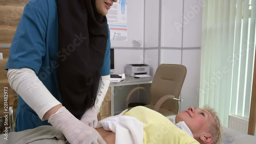 Female Muslim doctor wearing hijab and medical uniform doing palpation of female patient abdomen photo