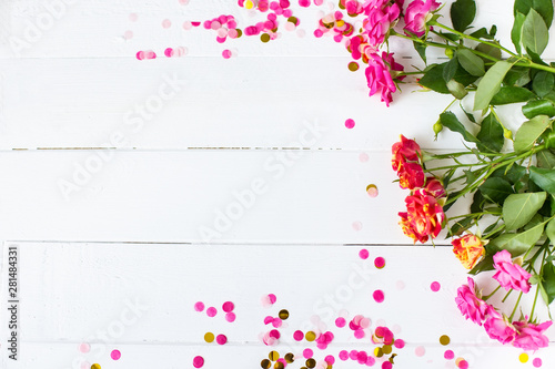 Flower frame with pink roses and confetti on wooden white background Wedding, birthday concept