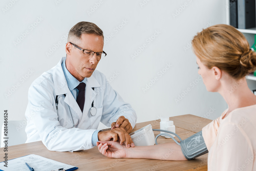 Fototapeta premium selective focus of handsome doctor in glasses measuring blood pressure of woman