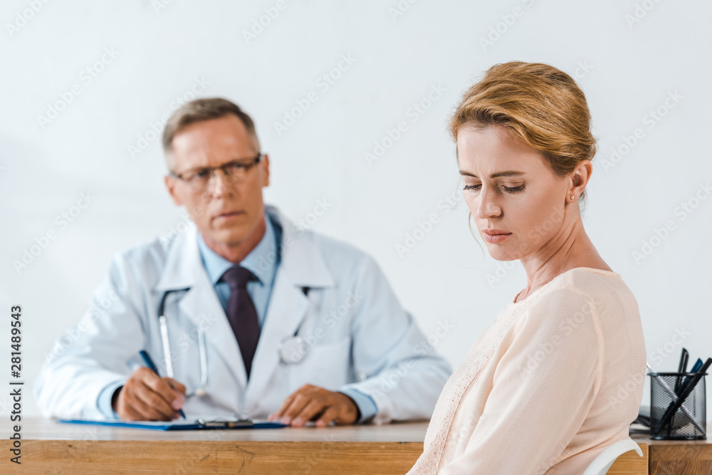 selective focus of sad woman sitting near doctor in white coat selective focus of sad woman sitting near doctor in white coat