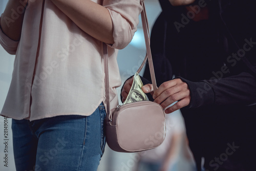 Cropped view of thief stealing dollar banknotes from bag of woman