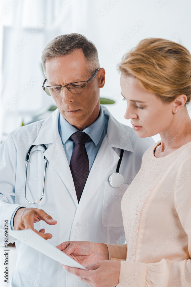 doctor in glasses pointing with finger at document near woman doctor in glasses pointing with finger at document near woman