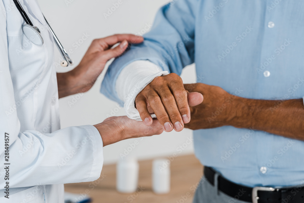 cropped view of doctor touching broken arm on man in clinic cropped view of doctor touching broken arm on man in clinic