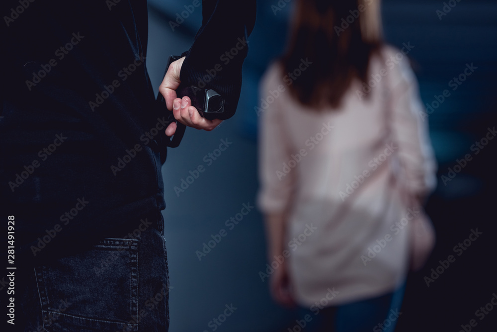 selective focus of robber holding gun behind walking woman