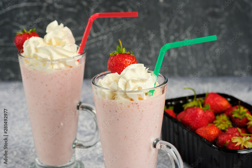 Two glasses with strawberry milkshake with pieces of berries on the edge of the glass on gray background. Two glasses with strawberry milkshake with pieces of berries on the edge of the glass on gray background.