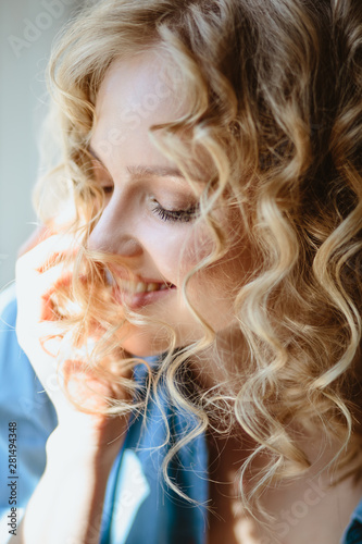 Close up portrait of blonde charming young woman with curly hair and natural makeup. Sunny morning, spa and care