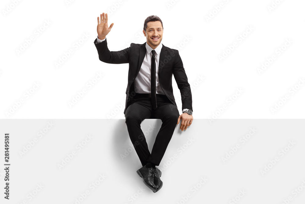 Young man in a suit sitting on a panel and waving at the camera Young man in a suit sitting on a panel and waving at the camera