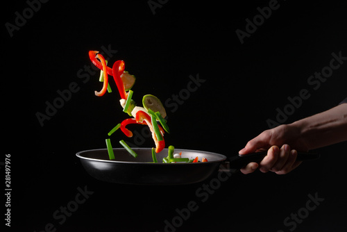 Close-up, chef preparing vegetables in a skillet frying them. Hotel business and the menu in restaurants, the book of recipes. On a black background